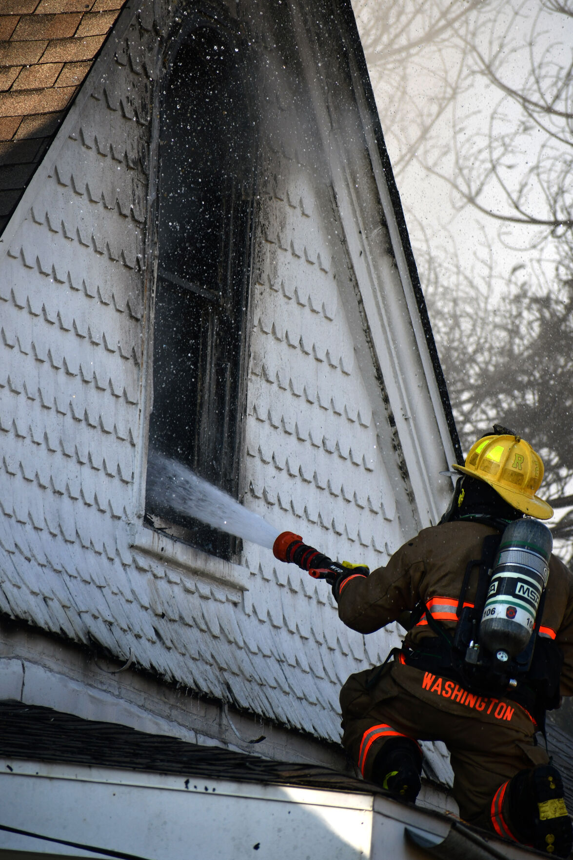 A firefighter uses a hose on the roof